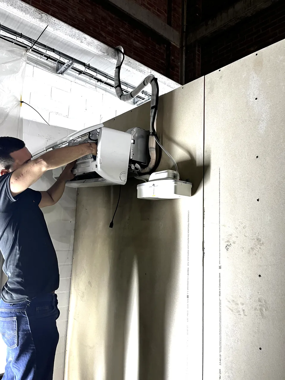 Técnico de RSI instalando la unidad interna de un aire acondicionado en una pared de drywall, con la tubería aislada hasta el cielo raso