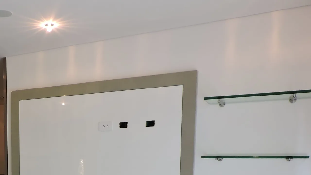 Detalle de acabados interiores: luminaria empotrada encendida en el cielo raso, panel enmarcado con salidas eléctricas y de datos, y repisas de vidrio
