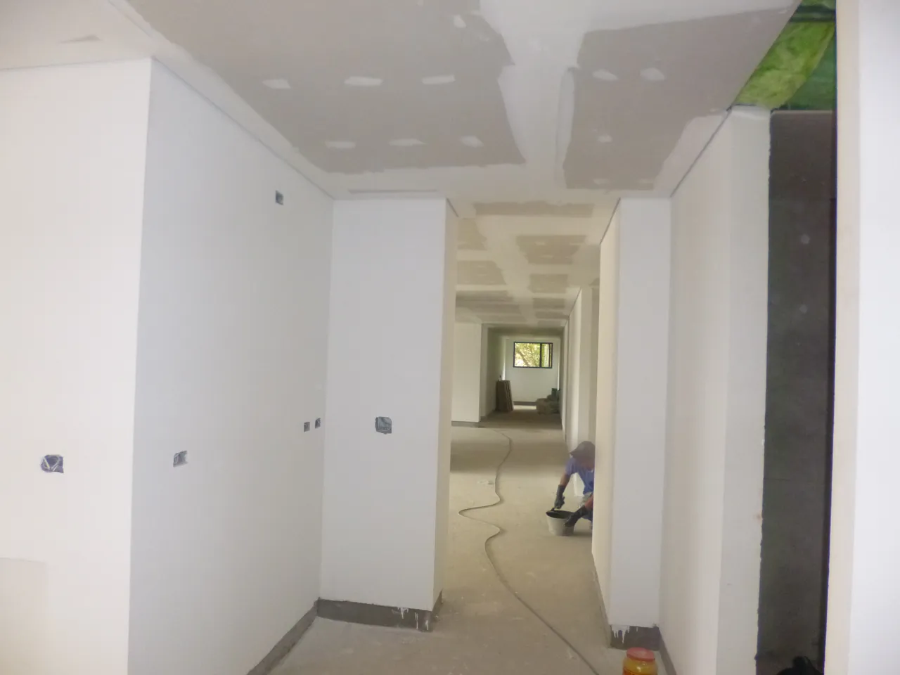 Pasillo en obra con muros y cielo raso de drywall masillados, cajas eléctricas a la vista y el piso sin acabado