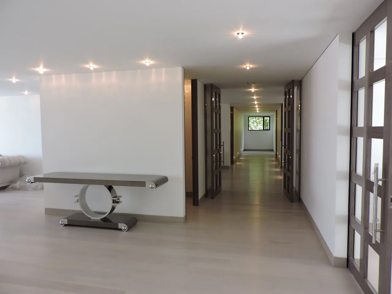 El mismo pasillo terminado, con piso de madera, puertas instaladas e iluminación empotrada encendida